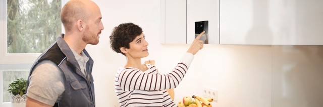 Mujer utilizando su nueva caldera Vaillant junto a un técnico Mujer utilizando su nueva caldera Vaillant junto a un técnico