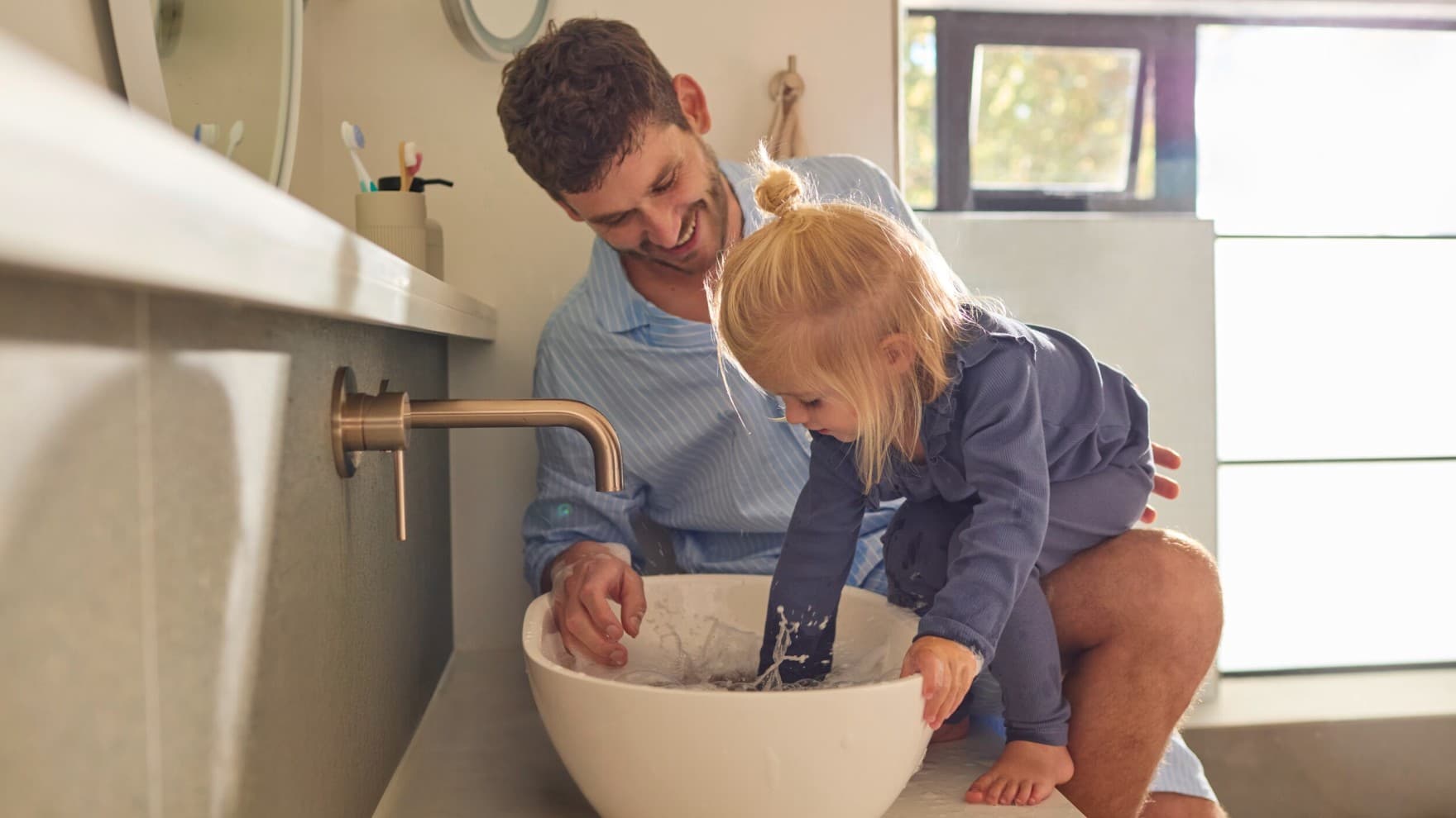 Un padre y una hija jugando con agua en un fregadero.
