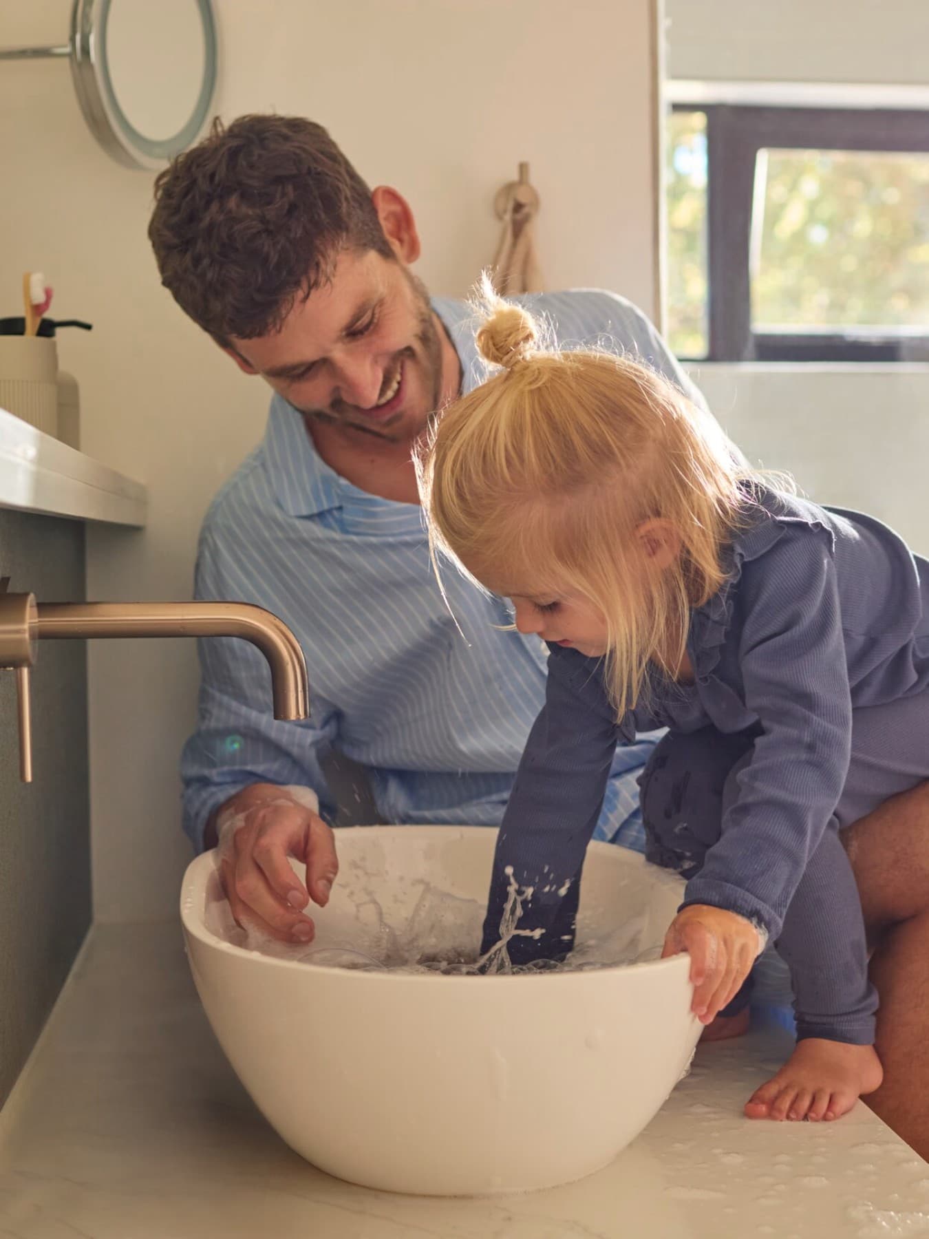 Un padre y una hija jugando con agua en un fregadero.