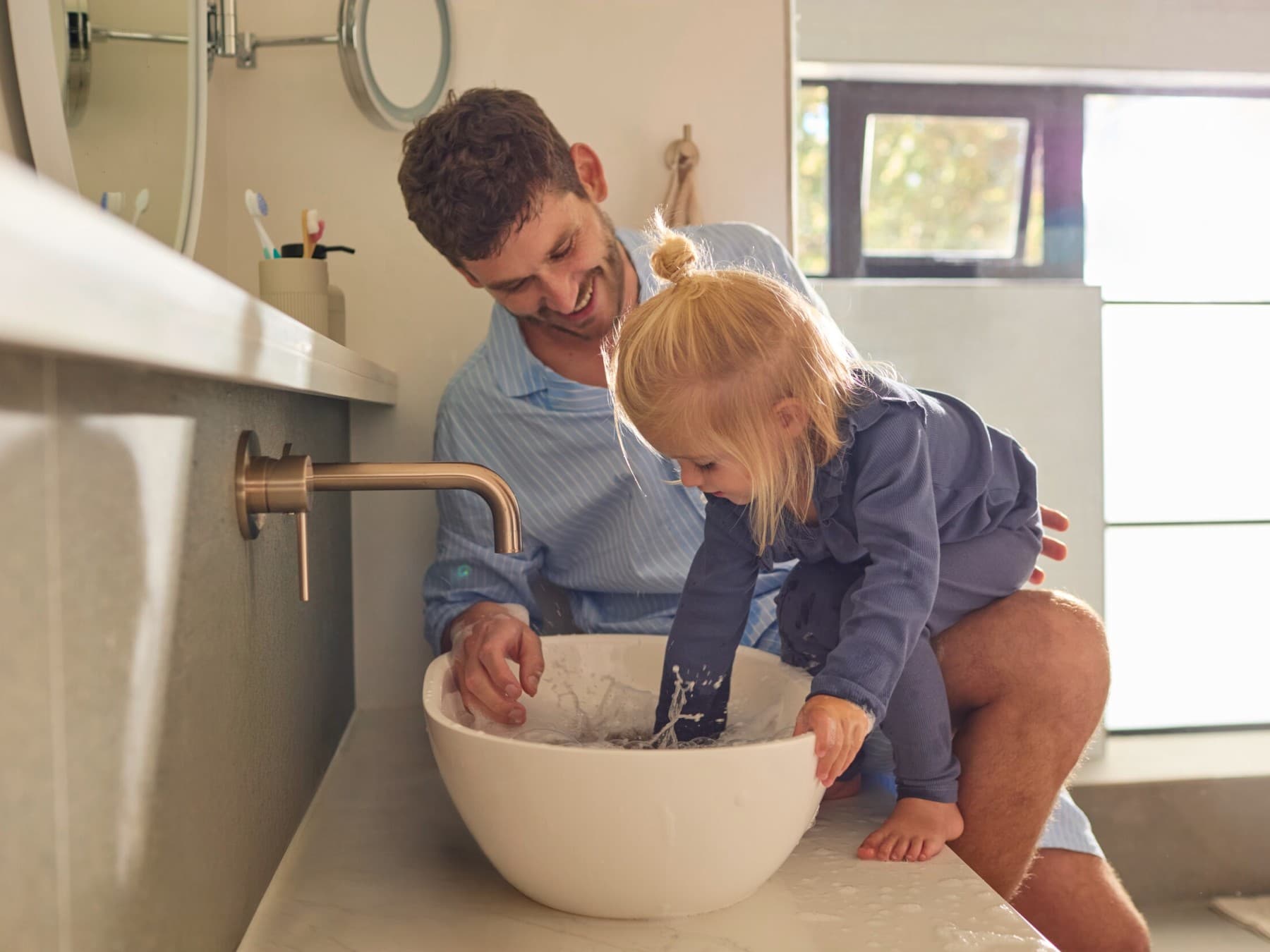 El padre y la hija están delante del lavabo del cuarto de baño jugando con el agua.