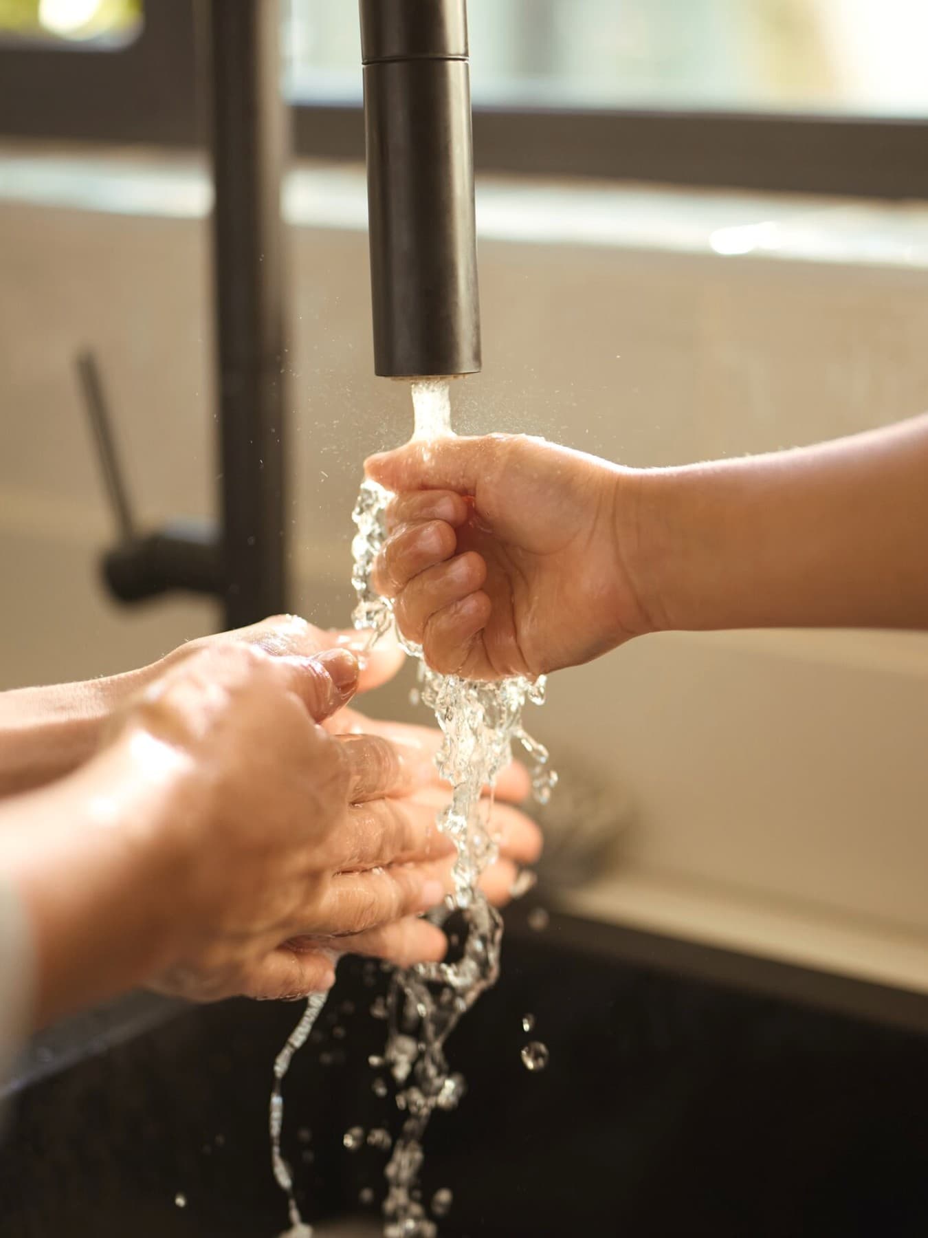 Mujer y niño sosteniendo sus manos bajo el agua corriente.