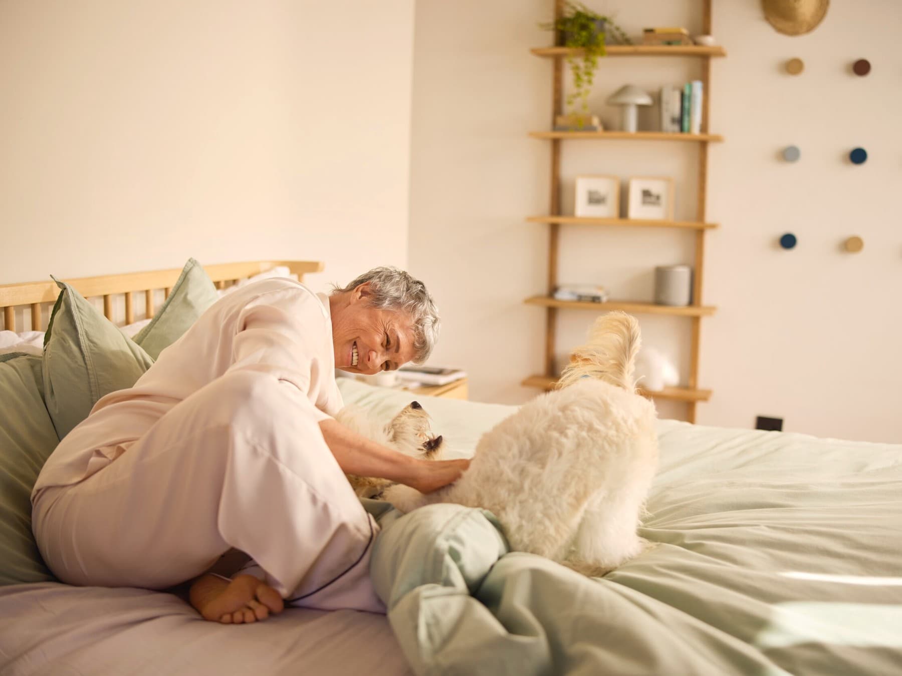 Una mujer sonriente acariciando a un perro en una cama.