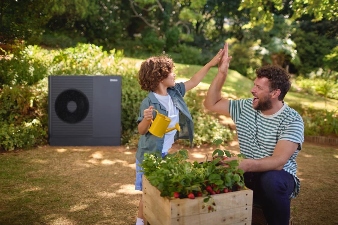 Padre e hijo disfrutan de su jardín con la nueva aroTHERM plus ES al fondo