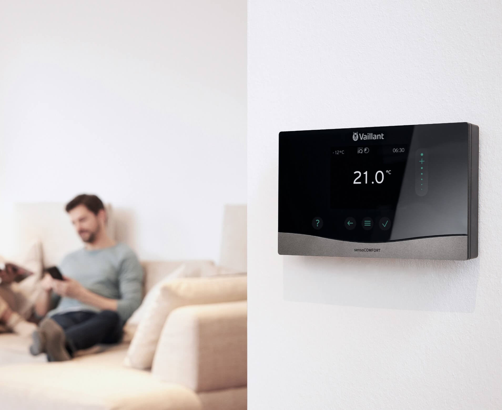 Heating control on wall with man on the couch in the background